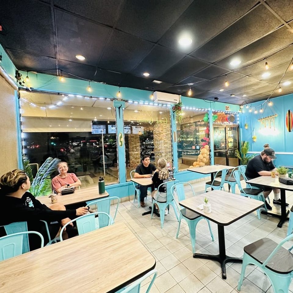 Diners seated at light wood tables with turquoise chairs inside Big Bros Hawaiian Grill, with string lights.