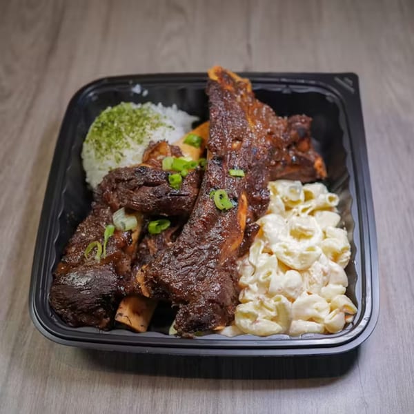 Hawaiian short ribs with rice and macaroni salad in a black takeout container on a wooden table.