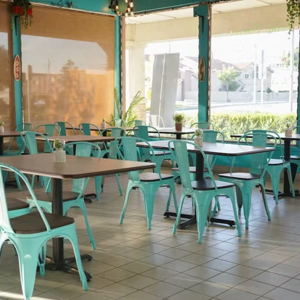Interior of Big Bros Hawaiian Grill with empty tables and bright turquoise chairs, large windows overlooking outside.